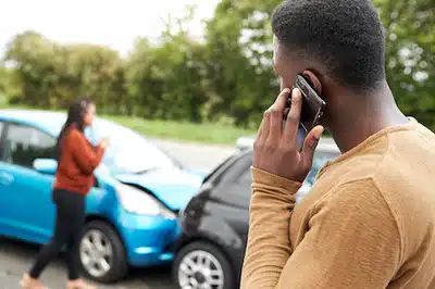 man on his phone looking at a car crash on the background