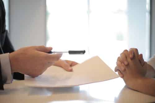 hand of a office worker handing a person a pen and care plan on a paper