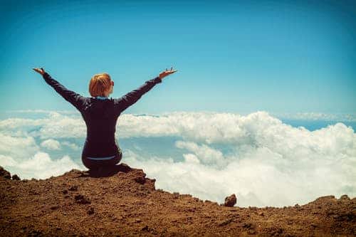 woman's back shot sitting on a mountain edge feeling great and energized