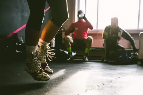 mid jump shot of legs with two guys in the background inside a gym